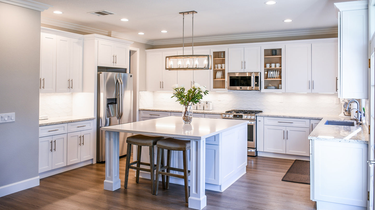 Bright and modern kitchen with white cabinets, a large central island with seating, stainless steel appliances, and elegant pendant lighting.