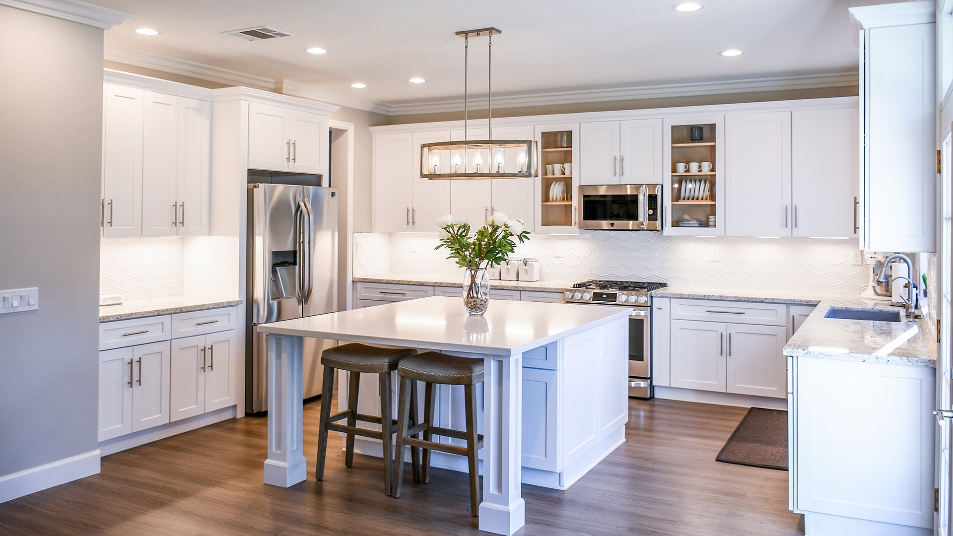 Bright and modern kitchen with white cabinets, a large central island with seating, stainless steel appliances, and elegant pendant lighting.