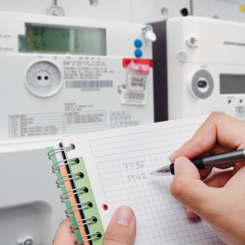 Person recording energy meter readings in a notebook, showcasing power usage tracking and efficiency monitoring.