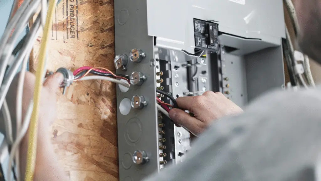 Person working on an electrical panel with various wires and connections visible.