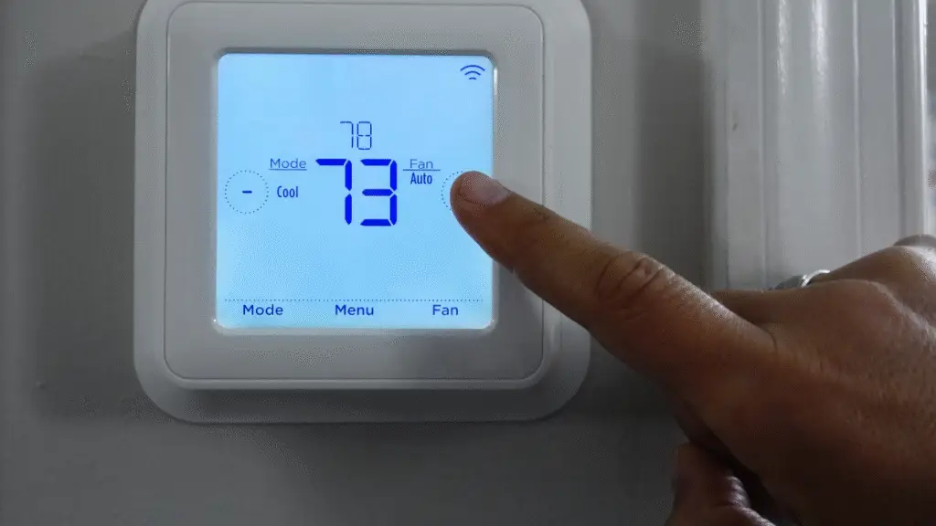 Digital thermostat showing a temperature setting of 73 degrees with a finger adjusting the controls.