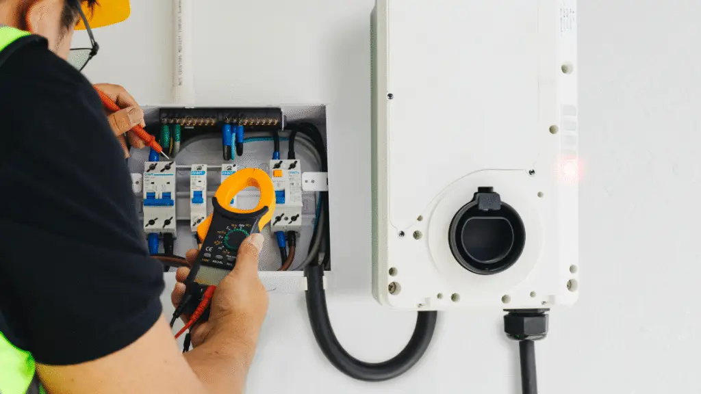 Electrician using a multimeter on an electrical panel with circuit breakers and a connected device.