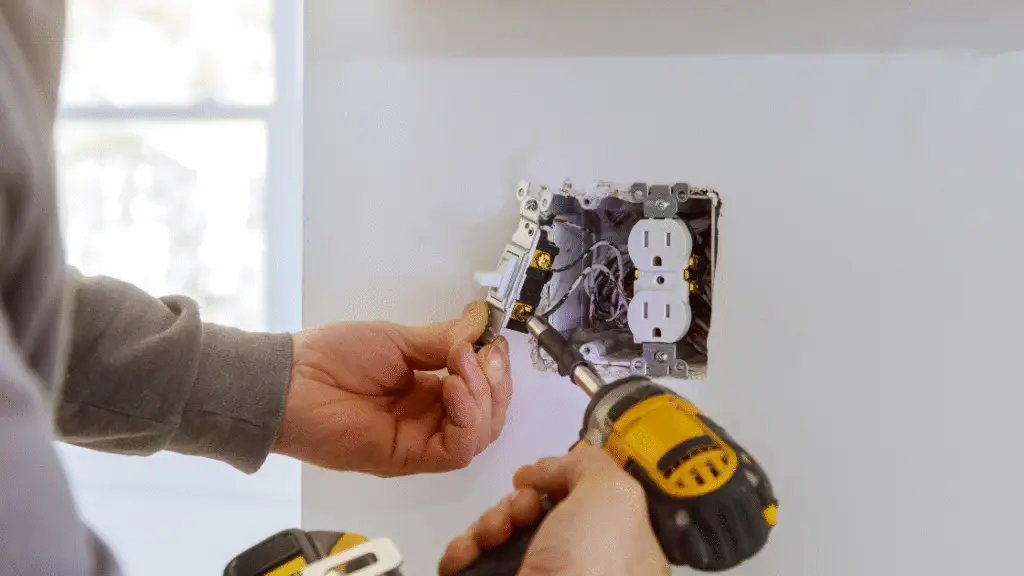 An electrician using a drill to install an electrical outlet in a wall.