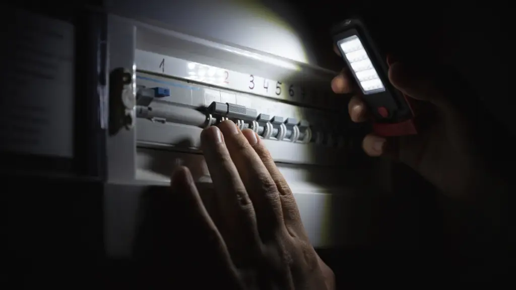 Individual using a flashlight to inspect a circuit breaker panel in low light conditions.