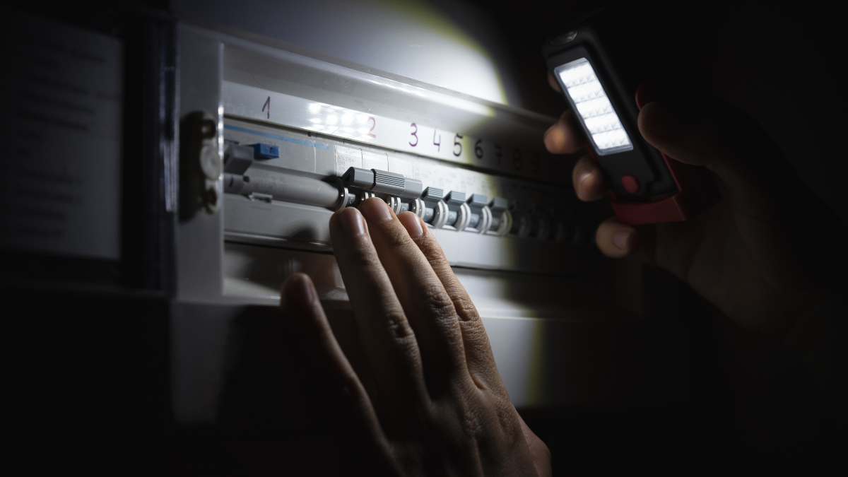 Individual using a flashlight to inspect a circuit breaker panel in low light conditions.